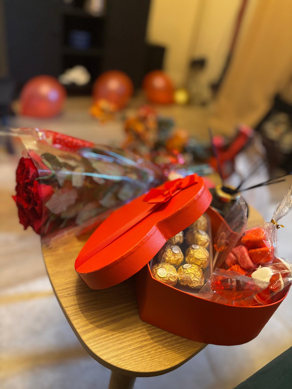 Chocolate and sweet gift box on the table, with roses and balloons in the background